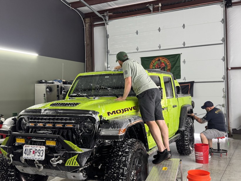 Two Auto Film Studio technicians hand-washing a foam-covered green Jeep Gladiator Mojave