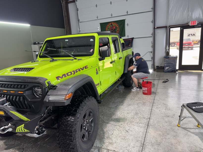 Technician cleaning the wheels and arches of a green Jeep Gladiator Mojave