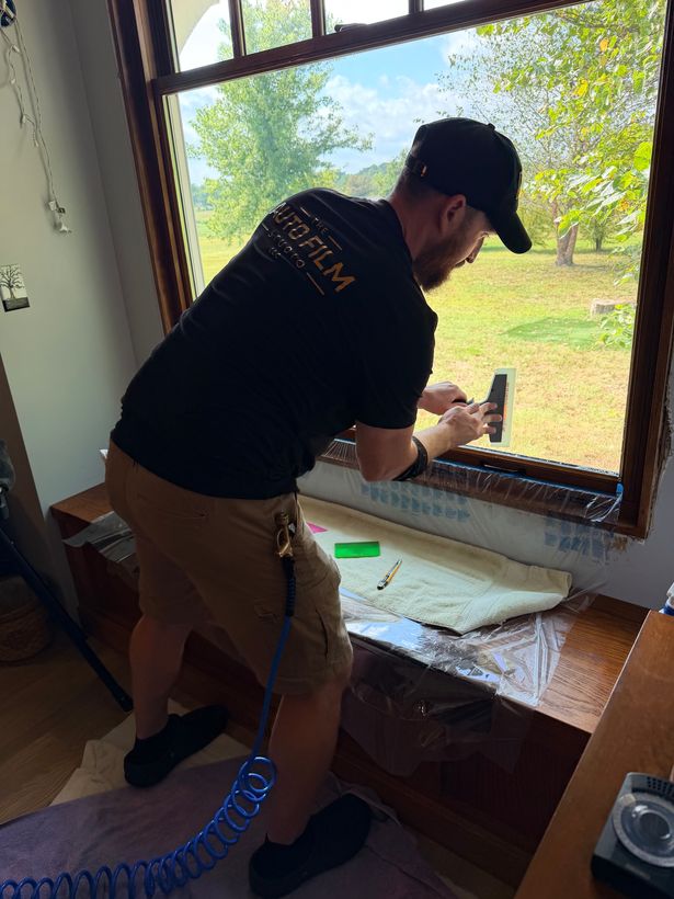 Auto Film Studio installer smoothing window film onto a large picture window inside a home