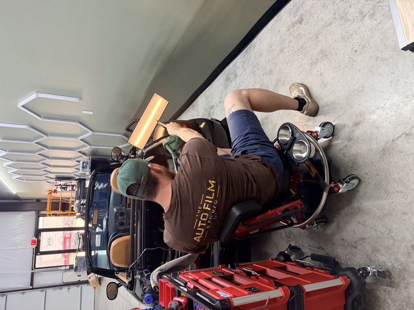 Auto Film Studio technician performing paintless dent repair on the rear quarter of a black Mazda Miata using a PDR light bar