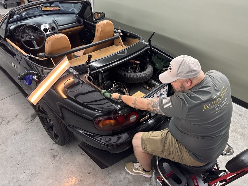Technician performing paintless dent repair on the rear quarter of a black Mazda Miata