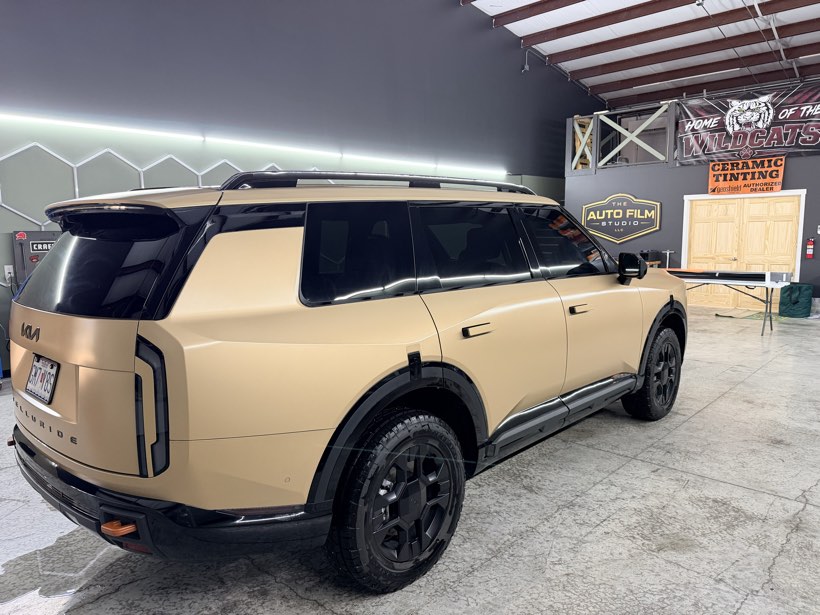Tinted matte sand Kia Telluride beside The Auto Film Studio and Ceramic Tinting shop signage